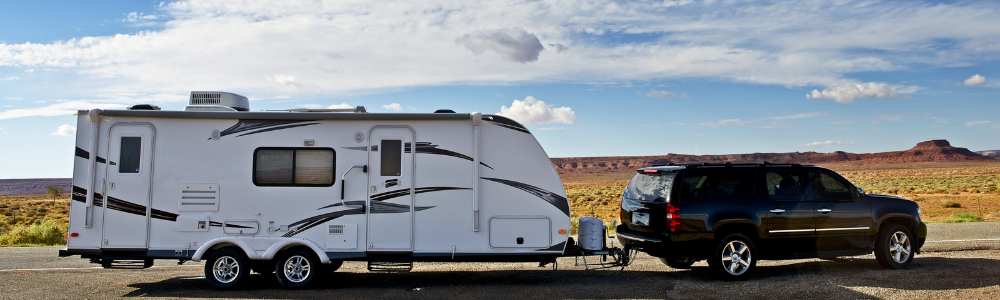 Vehicle towing an RV trailer on a desert road.